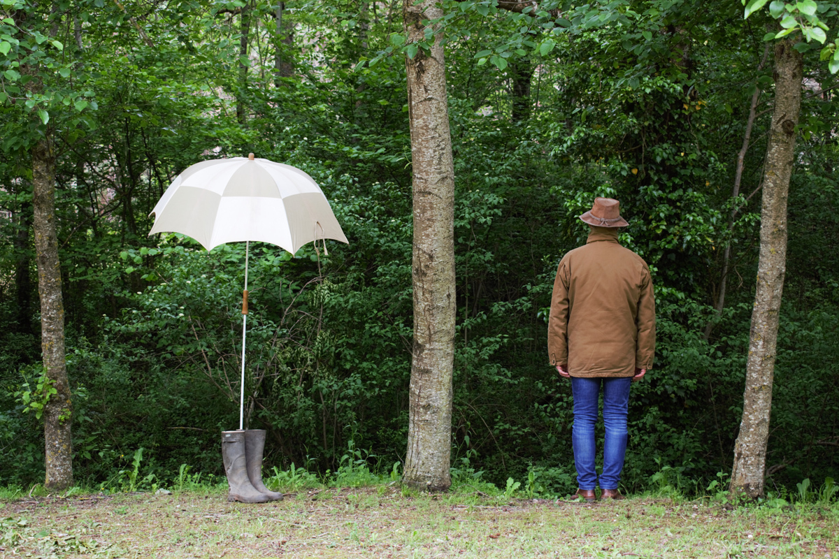 man standing between trees beside un umbrella in the boots